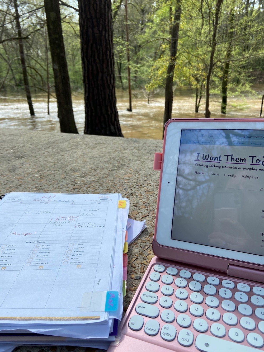 typing on iPad beside flooded river