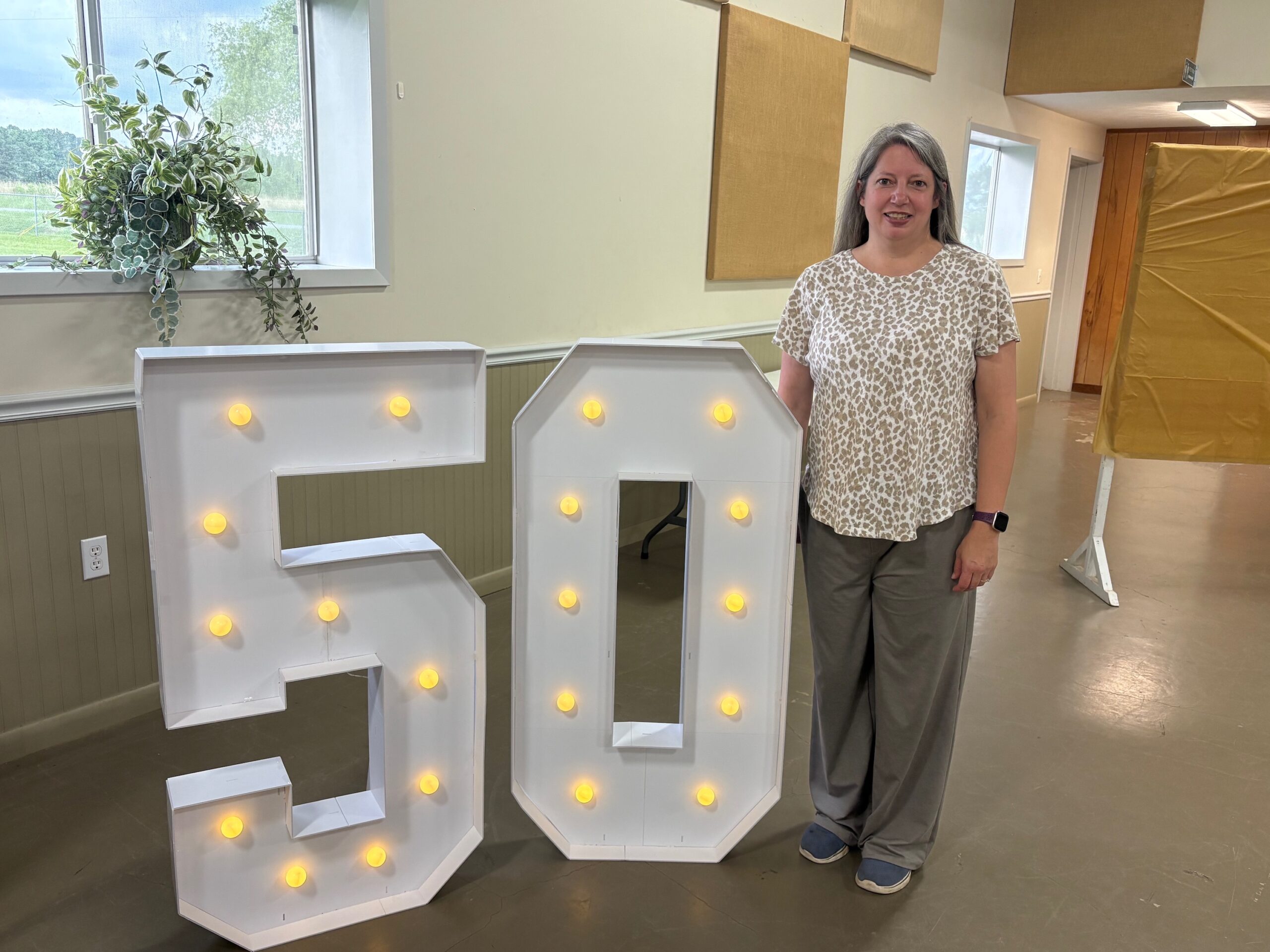Marsha Hays -woman standing beside large number 50 with lights
